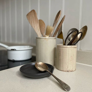 Two Victorian marmalade pots holding kitchen utensils alongside an enamel pan and a spoon rest